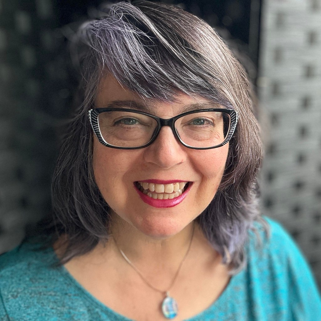 Izolda wearing turquoise top facing camera and with dark gray background